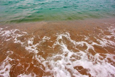 Deniz dalgasının yüzeyinde köpük ve hava kabarcıkları ve kumsalın kumlu kıyıları.