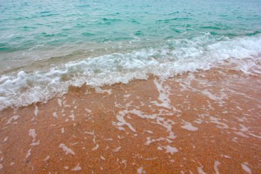 Deniz dalgasının yüzeyinde köpük ve hava kabarcıkları ve kumsalın kumlu kıyıları.