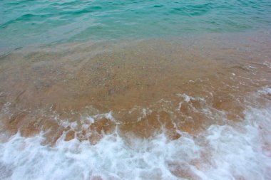 Deniz dalgasının yüzeyinde köpük ve hava kabarcıkları ve kumsalın kumlu kıyıları.