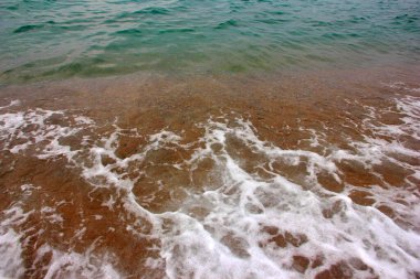 Deniz dalgasının yüzeyinde köpük ve hava kabarcıkları ve kumsalın kumlu kıyıları.