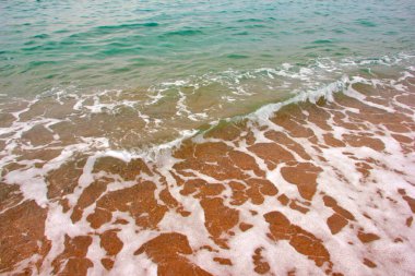 Deniz dalgasının yüzeyinde köpük ve hava kabarcıkları ve kumsalın kumlu kıyıları.