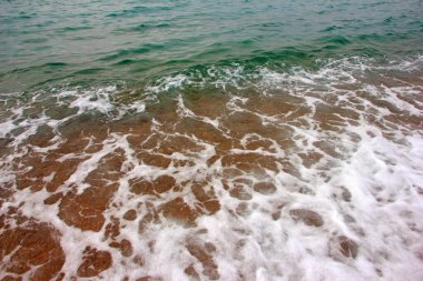 Deniz dalgasının yüzeyinde köpük ve hava kabarcıkları ve kumsalın kumlu kıyıları.