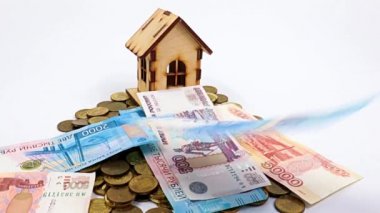Ahşap bir ev, metal ruble yığını üzerinde duruyor ve kağıt gagalar düşüyor.