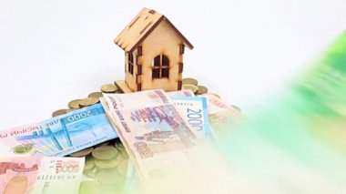 Ahşap bir ev, metal ruble yığını üzerinde duruyor ve kağıt gagalar düşüyor.