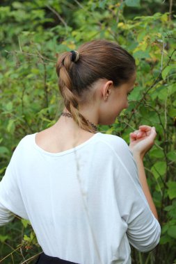 Uzun saçlı sarışın bir kız doğada oynuyor.