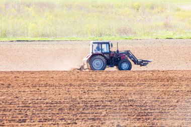 Güneşli bir bahar gününde traktör tarlayı sürüyor.