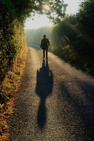 Homem caminhando ao longo de uma pequena estrada rural Imagens Royalty-Free