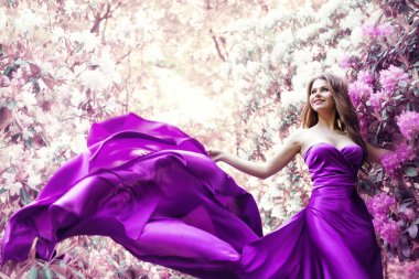 Bahar Çiçeği Bahçesinde Moda Kadını Pembe Elbisesi. Mor İpek Elbiseli Güzel Manken Kız Rüzgarda Çırpınıyor. Çiçek Pembesi Fantezi Arkaplanı