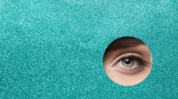 Eye Close up. Beauty Woman Eye Macro Make up. Green Pupil Eye Makeup Closeup looking out Hole Glitter Blue Paper. Eyelashes Extensions, Eyeliner, Eye Correction