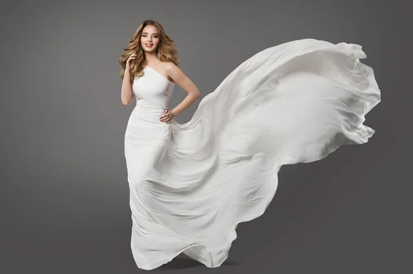 白いドレスの女性 グレーの背景に風に乗って飛んで結婚式のガウンの美しさの花嫁モデル ブライダルファッション服 カーリーヘアスタイルとメークアップ — ストック写真