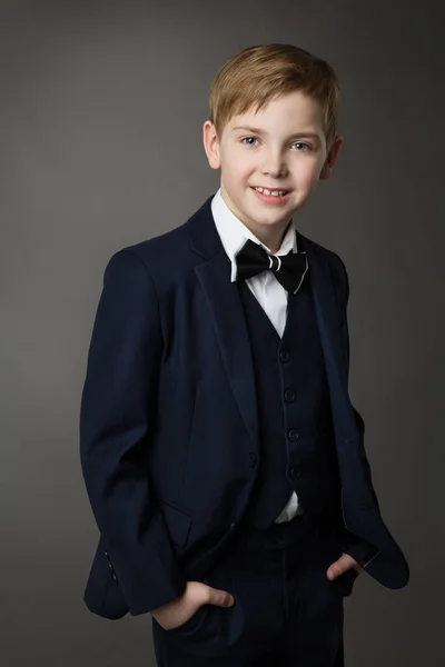 グレーの上に蝶ネクタイで古典的な黒のスーツでエレガントな小さな男の子 笑顔子供紳士でスマートカジュアル服 スクールキッズファッション — ストック写真