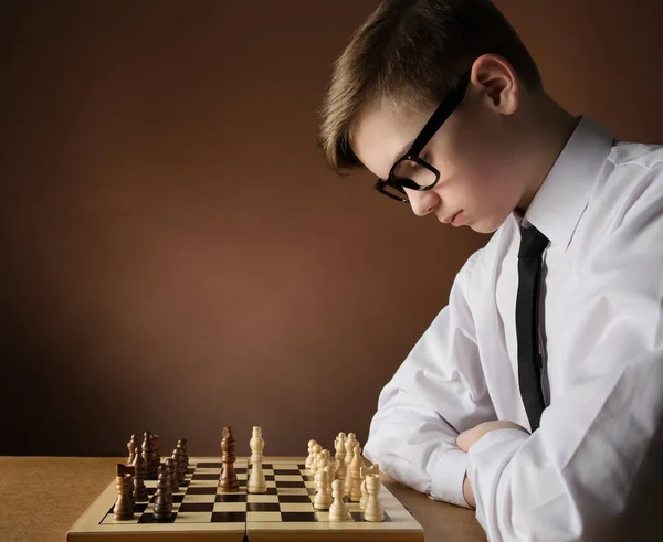 Chess Player Concentrate Thinking about Game Strategy at Chessboard. Young Boy playing boardgame over Dark Brown Studio Background. Side view