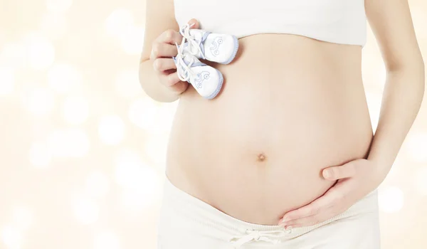 Estômago grávida e botas de bebê recém-nascido, Mulher mostrando barriga e botas recém-nascidas, Conceito de gravidez — Fotografia de Stock
