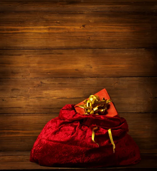 Santa Claus tašku, vánoční červený pytel na hnědé dřevěné pozadí — Stock fotografie
