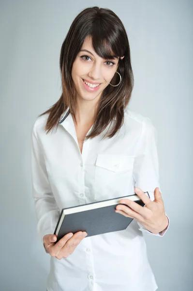 Morena sorridente em camisa branca com livro preto — Fotografia de Stock