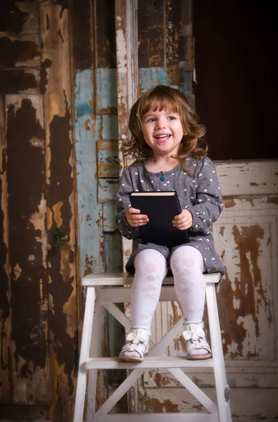Meisje, zittend op een stoel met een boek en lachen. Studio — Stockfoto