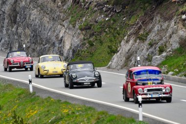 Kırmızı bir Volvo Pv544, koyu yeşil Daimler Sp250, sarı Porsche 356 ve kırmızı bir Alfa Romeo Giulia örümcek