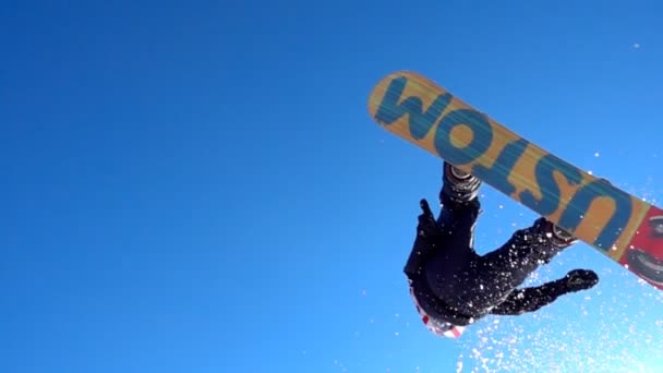 SLOW MOTION CLOSE UP: Snowboarder jumping over the camera spinning.