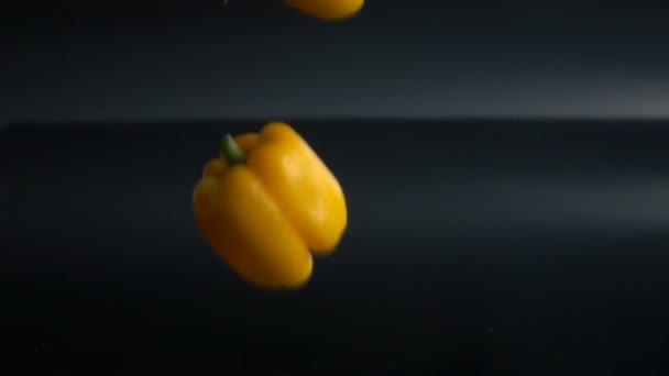 Yellow and red peppers falling on black background — Stock Video