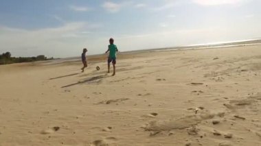 Bir kumsalda futbol topuyla oynayan çocuklar