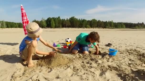 Dva chlapci, budování hrad z písku na pláži — Stock video