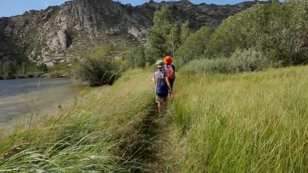 Pojkar gå med ryggsäckar längs sjön i bergen. — Stockvideo