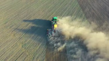 Alandaki traktörün hava görüntüsü. Yeşil traktör toprağı işliyor ve kuru bir tarlayı tohumluyor. Çiftçi tohum ekiciyle toprağı hazırlıyor. Çiftçilerin tarlalarında tarım ekimi için toprak hazırlanıyor..