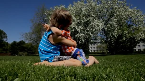 Happy little kids lying and hugging on green grass in spring park — Stock Video