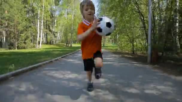 Ung pojke kör med fotboll på väg — Stockvideo