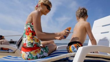 Genç ve güzel anne oğlunun sırtına güneş kremi sürüyor.