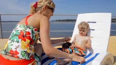 mutlu anne sandalyede oturan küçük çocuk güneş kremi uygulayarak