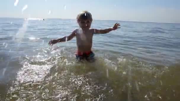 Щаслива дитина робить бризки в морі. Хлопчик весело води на відкритому повітрі . — стокове відео