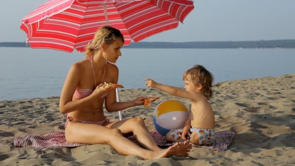 Mama karmi pizzę małe dziecko na plaży — Wideo stockowe