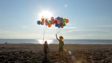 Çocuklar eğleniyor balonlarla sahilde güneşli bir günde atlama.