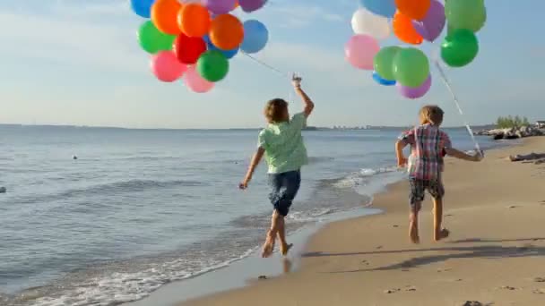 Garçons heureux avec de nombreux ballons colorés en cours d'exécution sur la plage — Video