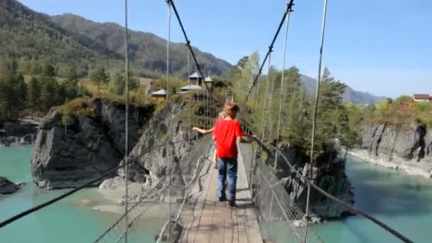 Young boy walking  through a rope bridge over the river in mountains to the Church. — Stock Video