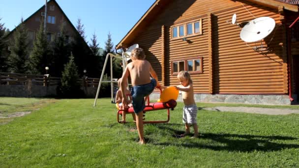 Enfants jouant sur l'aire de jeux près de la maison en bois . — Video