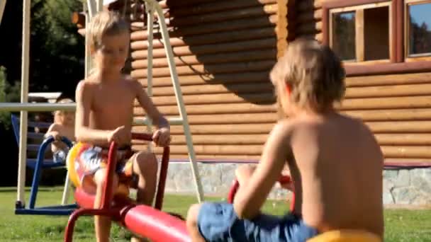 Счастливые дети играют на детской площадке возле деревянного дома — стоковое видео
