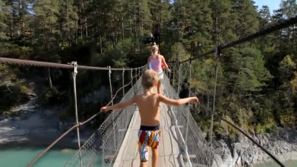 Criança e sua mãe caminhando através de uma ponte de corda sobre o rio nas montanhas . — Vídeo de Stock