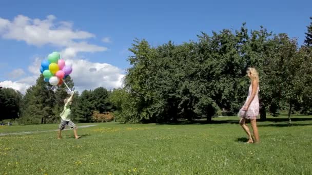 Kluk balónky své matce v parku na jaře. — Stock video