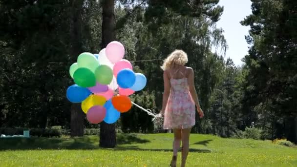 Jonge vrouw in jurk met veel kleurrijke ballonnen wandelen in het park — Stockvideo