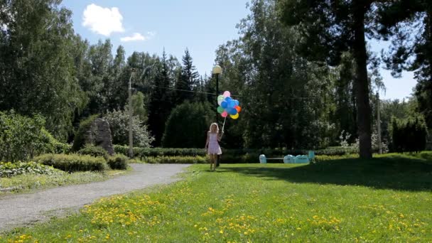 Jeune femme en robe avec de nombreux ballons colorés marchant dans le parc verdoyant — Video