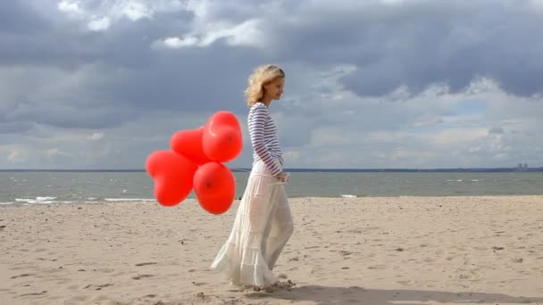 Jeune femme avec des ballons à coeur rouge debout sur la plage — Video