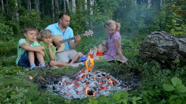 Rodzina siedzi przy ognisku w lesie i zabawy. — Wideo stockowe