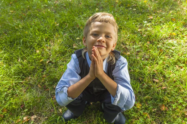 Sonriente niño sentado en la hierba verde — Foto de Stock
