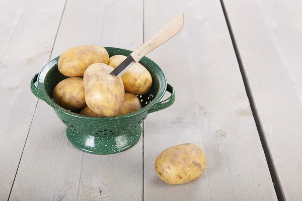 Peeling potatoes in colander with knife — Stock Photo, Image