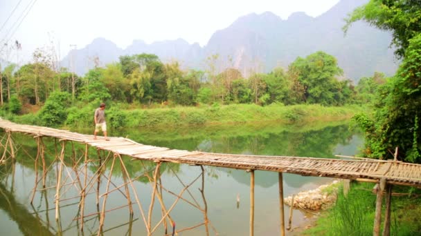 Man kruising rivier op bamboe brug — Stockvideo