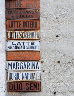 Güney İtalya 'da bir sokakta ekmek, yağ, süt, peynir, tereyağı ve margarin için paslı metal reklam levhası