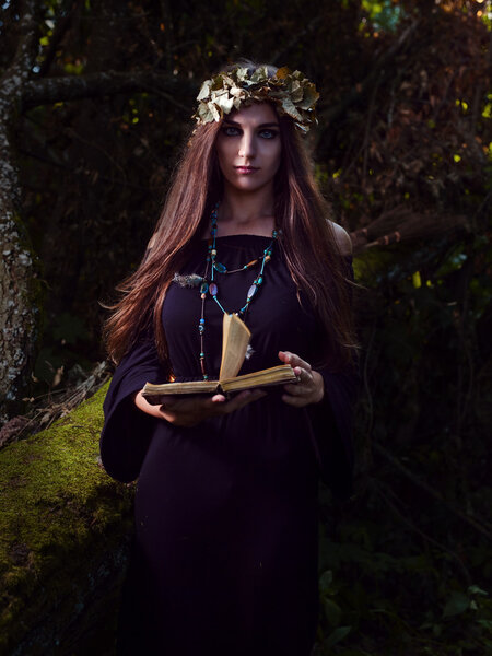 Young beautiful woman with book in dark forest
