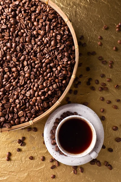 Taza de café negro y frijoles sobre un fondo dorado — Foto de Stock